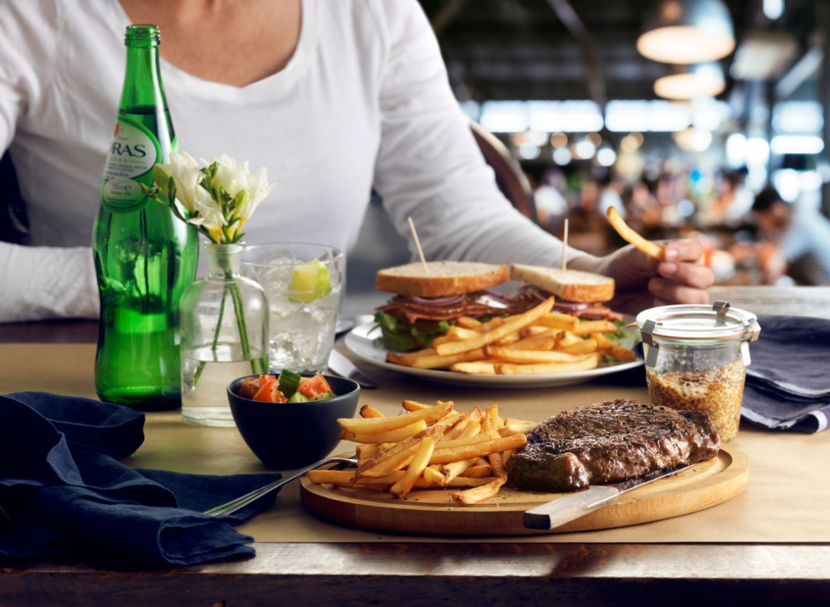 Lady enjoying a sandwich and Cavendish fries while another unseen guest eats fries and steak